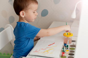 Little boy is painting colorful picture with gouache.