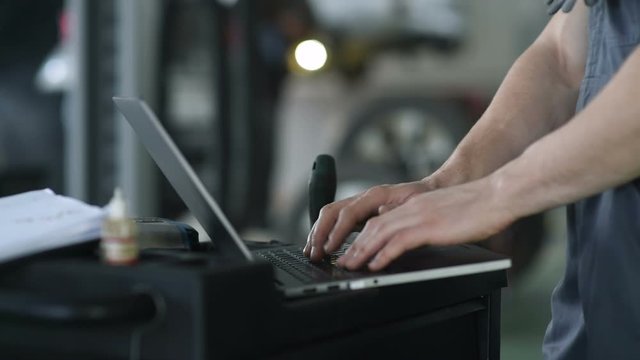 Car mechanic working on laptop in auto repair service.