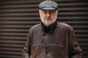 Handsome elderly man in leather jacket stands in front gate