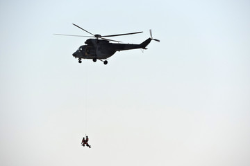 Two people hanging on a rope hanging from a rescue military helicopter, blue sky in the background