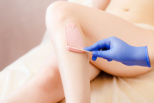 Close-up Of A Beautician Depilation With Hot Wax Woman's Leg In Beauty Spa. Body hair removal. Hair removal process on female leg with epilation.