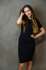 Vertical photo style girl with beautiful long hair in a black dress on a gray background in the studio