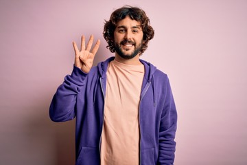 Young handsome sporty man with beard wearing casual sweatshirt over pink background showing and pointing up with fingers number four while smiling confident and happy.