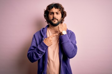 Young handsome sporty man with beard wearing casual sweatshirt over pink background In hurry...