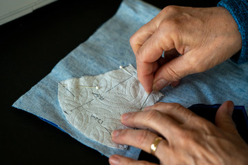 A closeup shows a woman's hands pinning a pattern into fabric for a covid-19 coronavirus protection face mask.