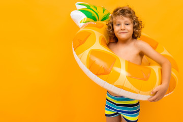 Little boy with curly hair in swimsuit with big rubber circle isolated on yellow background