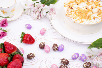 Cake covered with white cream and nuts, strawberries and chocolate eggs in a multi-colored falge.