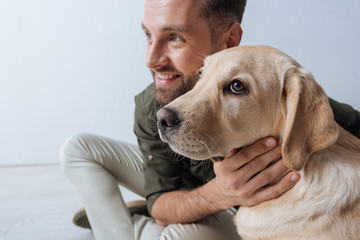 Selective focus of golden retriever sitting near smiling man on white background