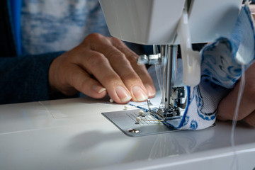 A seamstress makes a homemade covid-19 coronavirus sewing mask on a sewing machine.