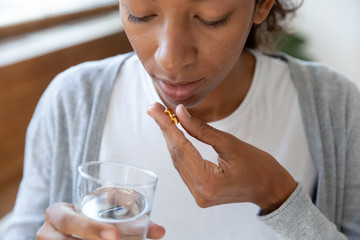 Close up of african american woman hold pills and glass of water in her hands. Take vitamin d...