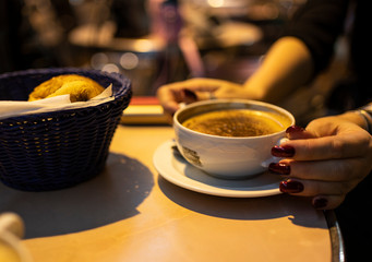 A cup of hot chocolate in female hands and a fresh croissant in a basket on a coffee table