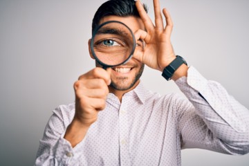 Young detective man looking through magnifying glass over isolated background with happy face smiling doing ok sign with hand on eye looking through fingers