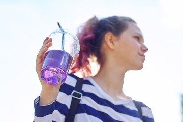Teen girl holding glass with straw with purple drink in hand