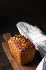 Homemade crusty loave of bread with pumpkin seeds on wooden background. Still life concept. Dark mood