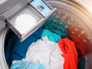 Top view of detergent in washing machine compartment with dirty colored clothes for washing.