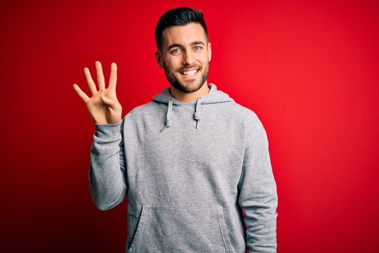 Young handsome sportsman wearing sweatshirt standing over isolated red background showing and pointing up with fingers number four while smiling confident and happy.