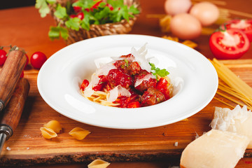 Italian pasta. Spaghetti with tomato sauce and meatballs on white plate with parmesan cheese, fresh parsley and tomatoes on rustic wooden background.
