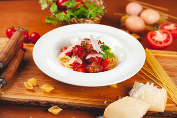 Italian pasta. Spaghetti with tomato sauce and meatballs on white plate with parmesan cheese, fresh parsley and tomatoes on rustic wooden background.