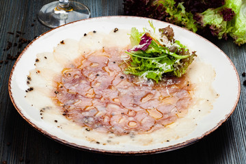 Seabass carpaccio served with arugula leaves, parmesan cheese and lettuce salad on white plate.