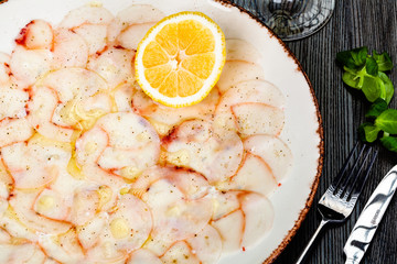 Octopus carpaccio with lemon on white plate.