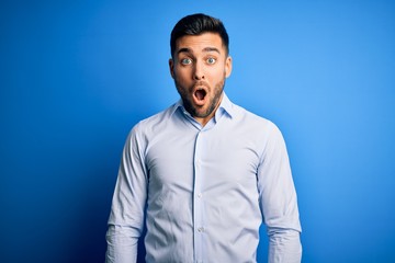 Obraz premium Young handsome man wearing elegant shirt standing over isolated blue background afraid and shocked with surprise expression, fear and excited face.