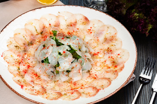 Dorado fish carpaccio served with arugula salad on white plate.