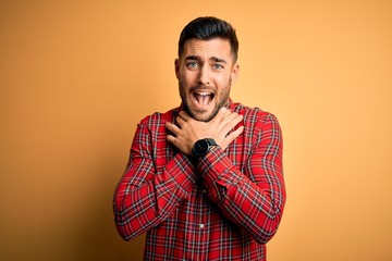 Fototapeta premium Young handsome man wearing casual shirt standing over isolated yellow background shouting and suffocate because painful strangle. Health problem. Asphyxiate and suicide concept.