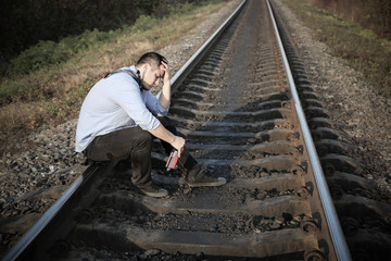 Man with alcohol on railway tracks outdoors. Depression disease. Economy crisis, poverty,...