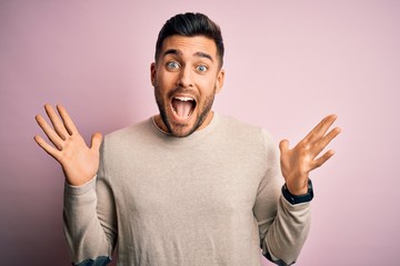 Fototapeta premium Young handsome man wearing casual sweater standing over isolated pink background celebrating crazy and amazed for success with arms raised and open eyes screaming excited. Winner concept