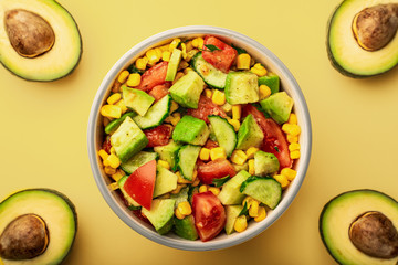 Top view bowl of avocado and tomato salad with cucumbers on a yellow background