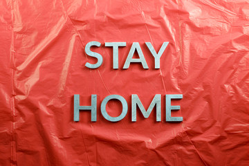 the words stay home laid with silver metal letters on crumpled red plastic background in flat lay...