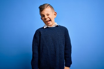 Young little caucasian kid with blue eyes wearing winter sweater over blue background winking...