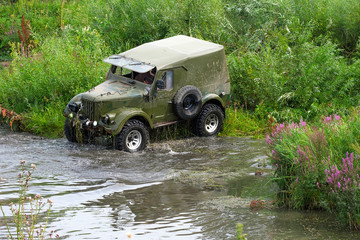a green SUV on the Bank of the river is preparing to cross to the other side
