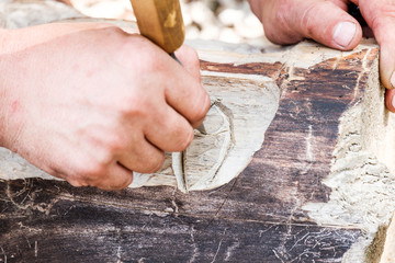 a wood carving master carves a line with a wood cutting tool on a log