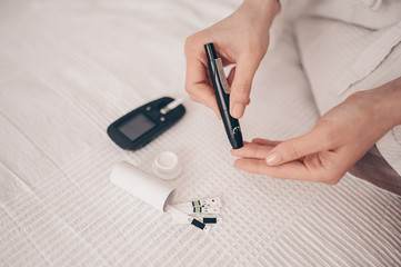 Diabetes checking blood sugar level. Woman using lancelet and digital glucometer at home. Medicine, diet diabetes, health care concept - female hands with glucometer checking body glucose level