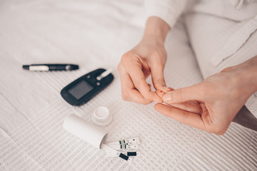 Diabetes checking blood sugar level. Woman using lancelet and digital glucometer at home. Medicine, diet diabetes, health care concept - female hands with glucometer checking body glucose level