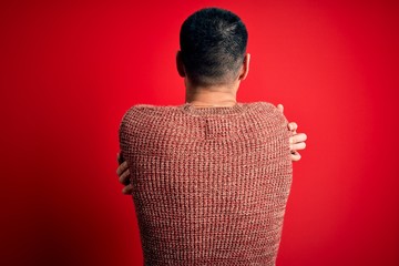 Young handsome hispanic man wearing nerd glasses over red background Hugging oneself happy and...