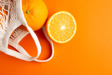 Cutting orange in cotton shopping eco friendly bag on orange background. Citrus harvest, monochrome composition