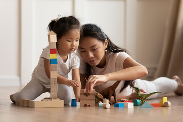 Involved little daughter her vietnamese mother play on warm floor using wooden colorful blocks...