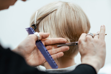 The work of a hairdresser. Hairdresser cut hair of a woman. Close-up of hands and tool
