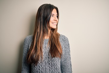 Young beautiful girl wearing casual sweater standing over isolated white background looking away to side with smile on face, natural expression. Laughing confident.