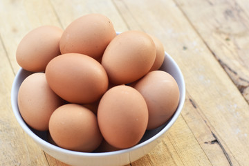 Brown chicken eggs in a white bowl on wooden table soft focus.