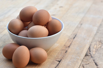Brown chicken eggs in a white bowl on wooden table soft focus.