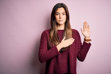 Young beautiful girl wearing casual sweater over isolated pink background Swearing with hand on...