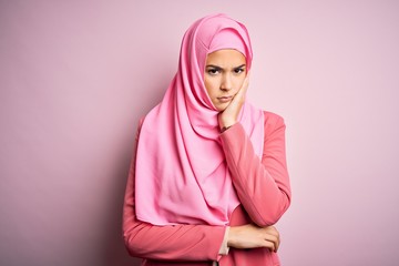 Young beautiful girl wearing muslim hijab standing over isolated pink background thinking looking tired and bored with depression problems with crossed arms.