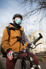 Obraz premium Young man on a bicycle in a medical mask in a city park.