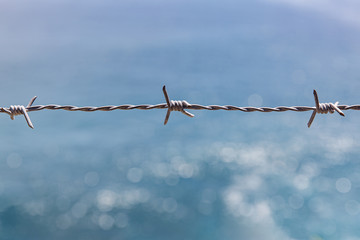 Barbed wire closeup. Blue sea on background.