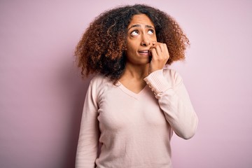 Young african american woman with afro hair wearing casual sweater over pink background looking stressed and nervous with hands on mouth biting nails. Anxiety problem.