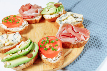 Traditional Italian bruschette snack on a wooden plate on a white wooden table and gray napkin. Mini sandwich mix. Close up