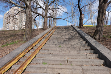 Empty old stairs with rusted metal rails without any people, which going up to the blue sky, surrounded by dry trees and typical ukrainian building in Kyiv, Ukraine